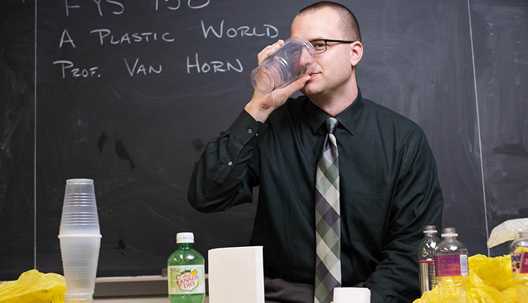Ryan Van Horn puts a plastic cup to his lips while surrounded by plastic products in a classroom.
