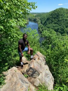 Basit Balogun '21 stands on a rock overlooking trees and a body of water.