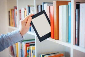 A person selection an ebook reader from a bookshelf that otherwise has books in it