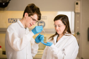 A student and professor in white lab coats work with a liquid in the polymers lab.