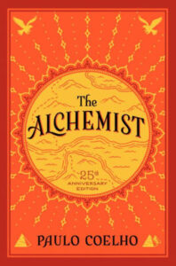 The cover of the book The Alchemist by Paul Coelho, with a sun in the middle and mountains and a stream on the sun
