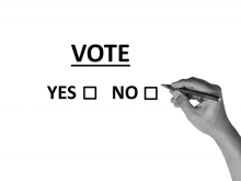 A hand with a pencil about to choose "yes" or "no" under the word "Vote"