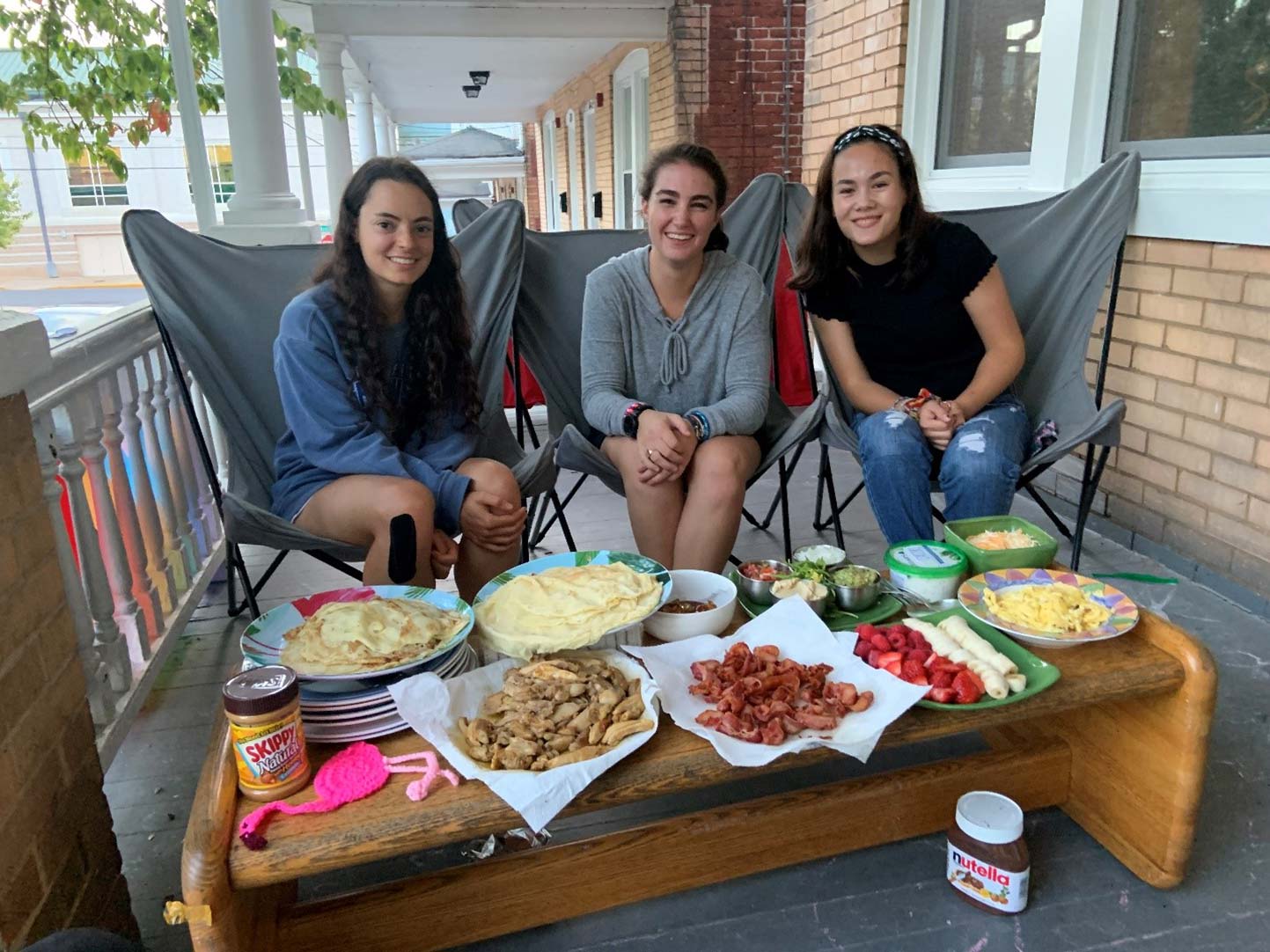 Rachel Hurley ’23, Anna Radcliff ’23 and Kellie Kottman ’23 sit on a couch behind a table filled with food at the Global Foods House in the Monroe Neighbhorhood.