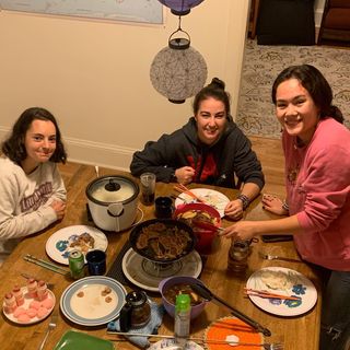 The three women in Global Foods House at the dinner table with plates, food, and smiles