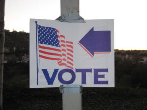 A sign with an arrow pointing to the American flag with the word Vote on the bottom