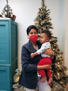 Alisha Gangadharan holds a baby in front of a Christmas tree.