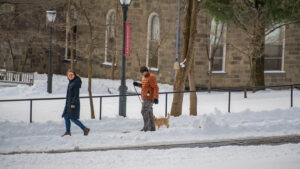 A man walks a dog in the snow with a woman walking nearby