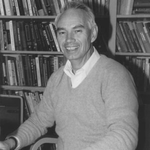 Howard Gallup sits in front of a bookshelf and smiles.