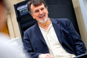 Prof. Tony Cummings stands in class, smiling while wearing a blue blazer and white collared shirt