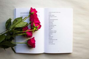 A book with a poem on the right page and several roses laying on top of the left page