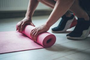 A person unrolls a pink yoga mat.