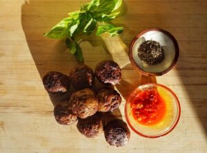 Meatballs, basil leaves, a dish of red sauce, and a dish of perhaps a condiment on a table