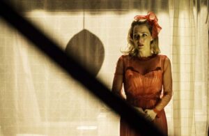 An actress portrays Blanche in A Streetcar Named Desire, wearing a red dress with sheer sleeves.