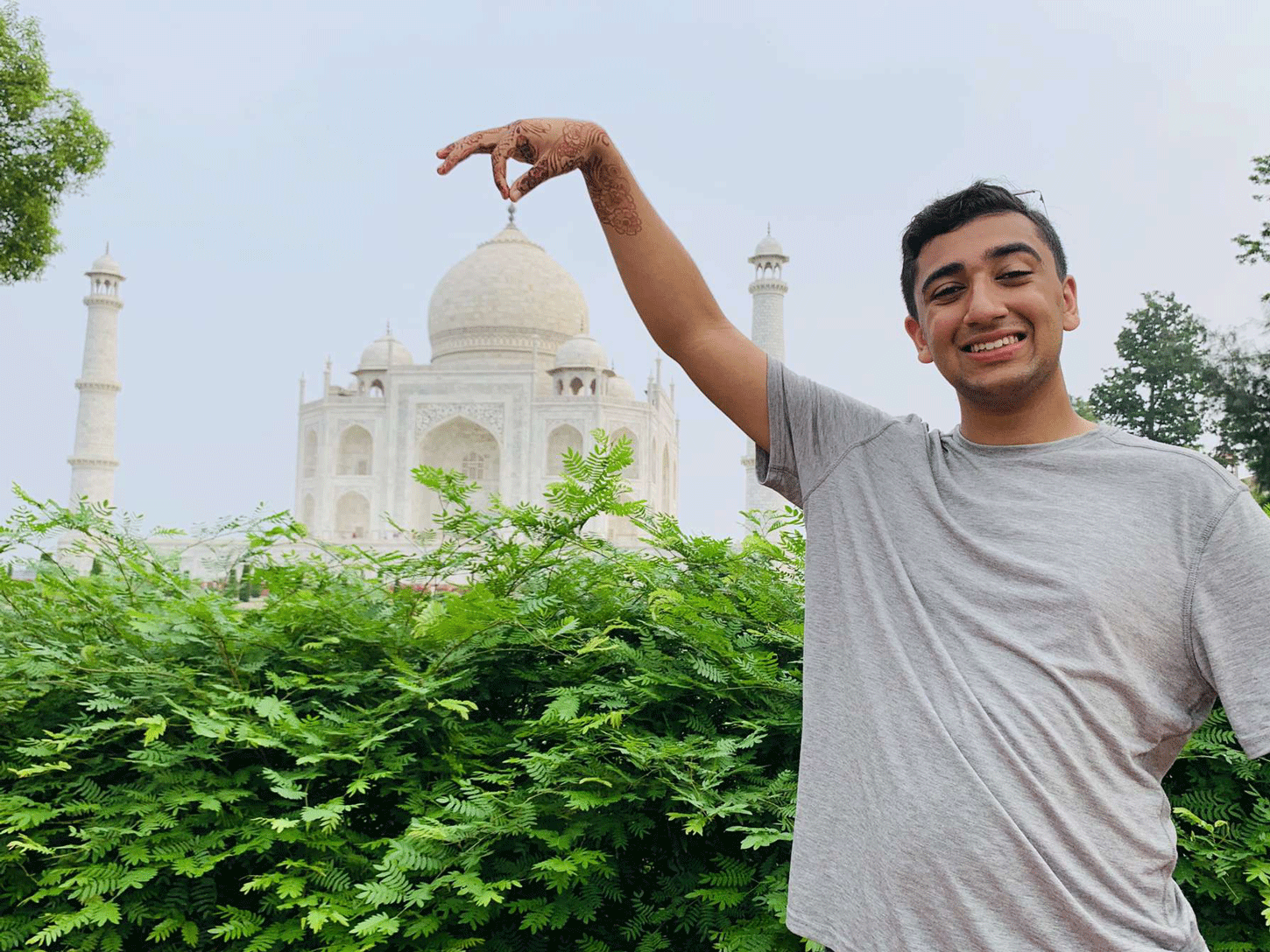 Zubair Ali stands far in front of a building and holds his thumb and index finger together to create the appearance that he's holding the building by its top