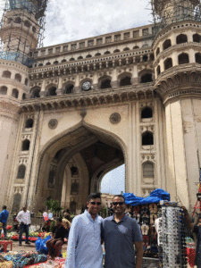 Zubair Ali and a companion pose for a photo in a market in India in front of a building's gateway