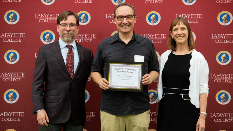 Alessandro Giovannelli holds his award while flanked by Provost John Meier and President Alison Byerly in front of a Lafayette-branded backdrop at Fisher Stadium.