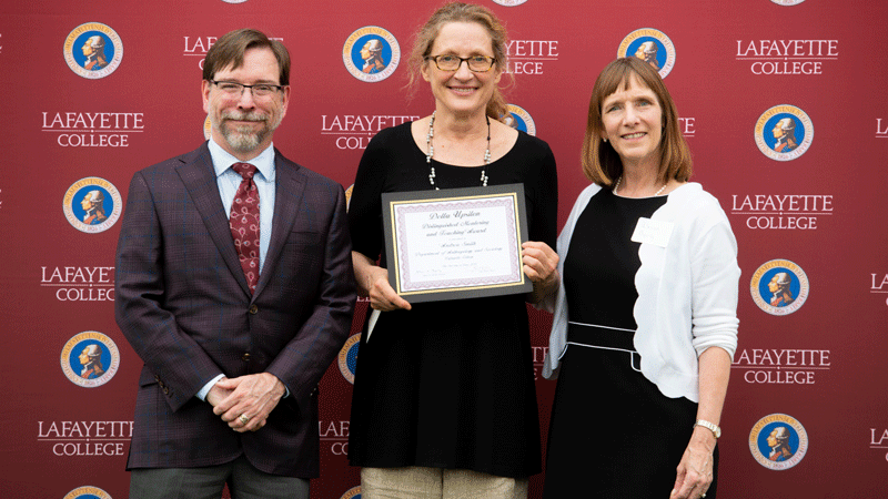 Andrea Smith holds her award while flanked by Provost John Meier and President Alison Byerly in front of a Lafayette-branded backdrop at Fisher Stadium.