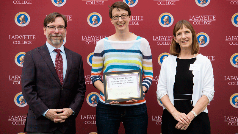 Julia Nicodemus holds her award while flanked by Provost John Meier and President Alison Byerly in front of a Lafayette-branded backdrop at Fisher Stadium.