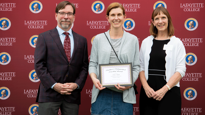 Julie Smith holds her award while flanked by Provost John Meier and President Alison Byerly in front of a Lafayette-branded backdrop at Fisher Stadium.