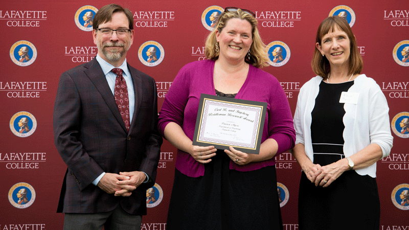 Lauren Myers holds her award while flanked by Provost John Meier and President Alison Byerly in front of a Lafayette-branded backdrop at Fisher Stadium.