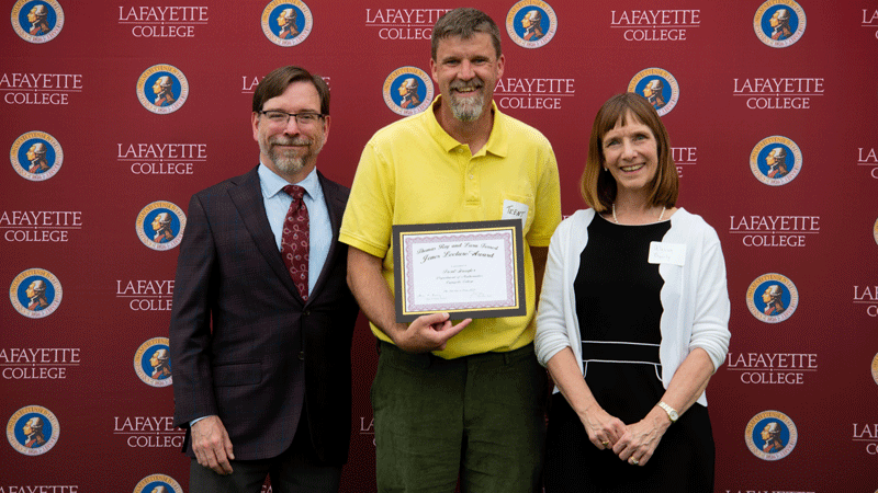 Trent Gaugler holds his award while flanked by Provost John Meier and President Alison Byerly in front of a Lafayette-branded backdrop at Fisher Stadium.