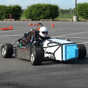 A student driver with a white helmet seated in a formula hybrid race car