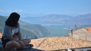 A student sits on a roof and looks at the mountains in the distance.
