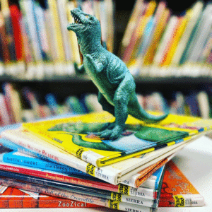 A toy Tyrannosaurus Rex dinosaur placed on a pile of children's books
