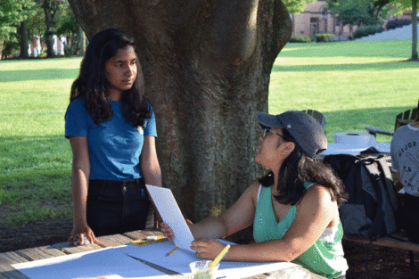 Student Tanushree Sow Mondal stands and talks with a student painter who is seated.