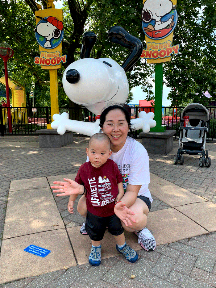 Tingting Kang with her young son in front of a big representation of Snoopy and two Camp Snoopy signs