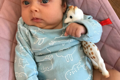 Baby Isabelle, daughter of Professor Annie de Saussure, in a onesie with drawings of sheep and holding a giraffe stuffed animal