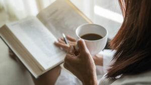 A woman reads a book while holding a cup of coffee.