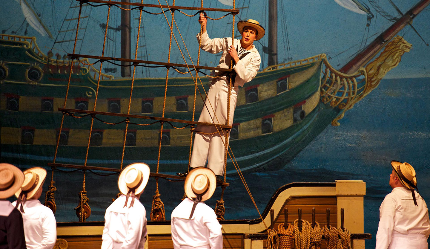 An actor stands on a pretend ship's rigging as he sings in H.M.S. Pinafore
