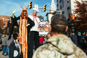 Two people on stilts wave at Bacon Fest in Easton, including a woman dressed as a piece of a bacon and a man in a chef outfit.