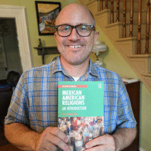 Professor Brett Hendrickson holds a copy of his new book, Mexican American Religions.