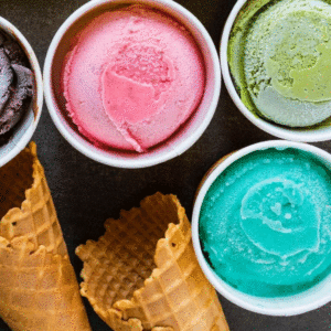 A few different flavors of ice cream in containers and a couple of ice cream cones