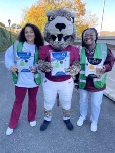 The Lafayette leopard stands with two students displaying the College's recycling and trash signage.
