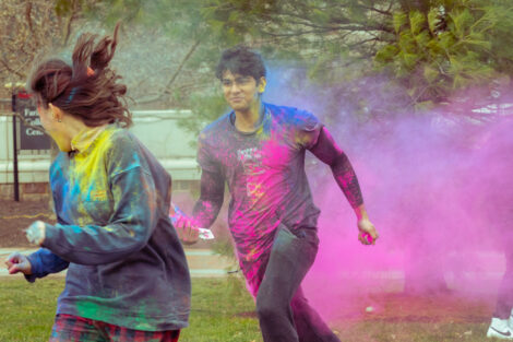 Two students run through a cloud of colorful powder during Holi Fest.