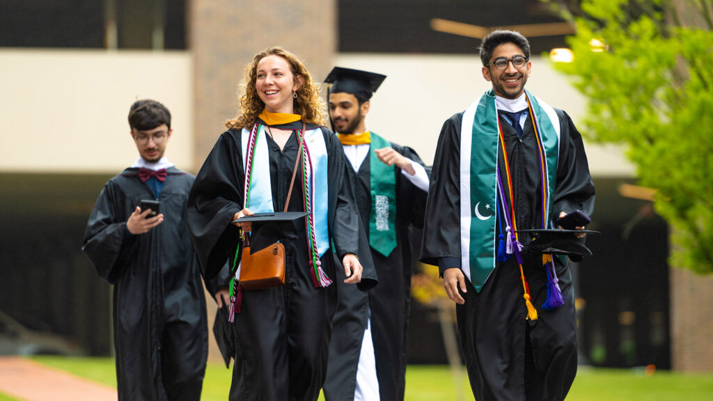 A group of four students walk across campus in their cap and gowns