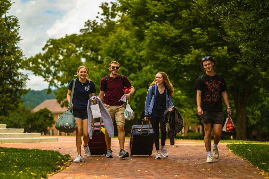 Four students wheel luggage into campus