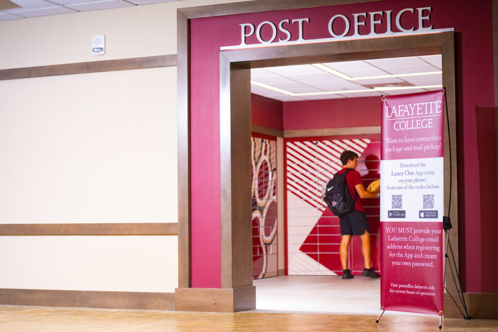 A view of the new Post office shows a maroon room with words Post Office. A student removes a package from lockers branded with a paw print and Lafayette colors.