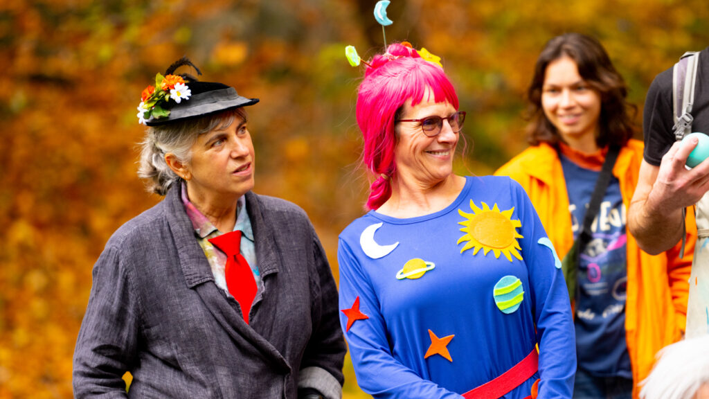 Two people smiling in costumes that feature flowers and images of the solar system.