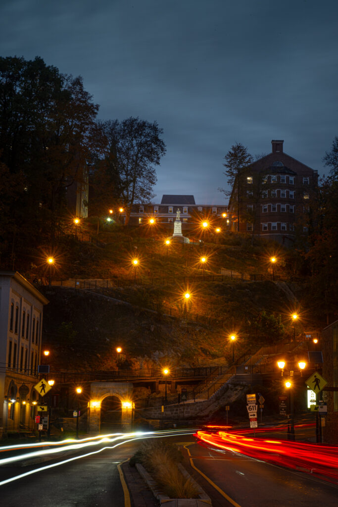 A view of the steps leading to South College from North Third St at Night. The long-exposure streaks of tail and head-lights are visible in the lower third of the frame. 