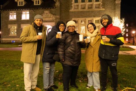 A group of Lafayette students and a staff member hold cups of cocoa on the Quad during the Quad Lighting.