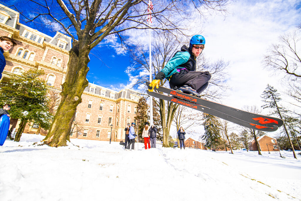 A student midair on skis behind Pardee Hall.