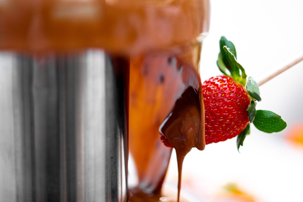 Close up of a strawberry being drenched by a chocolate fountain.