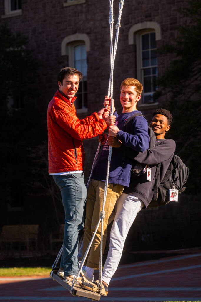 3 students standing on a swing smiling