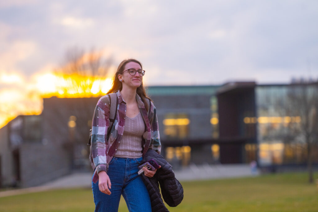 A person walks smiling at sunset with Skillman library in the background.
