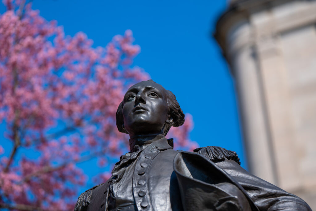 Close up of a statue of the Marquis de Lafayette with Cherry Blossoms in the background.