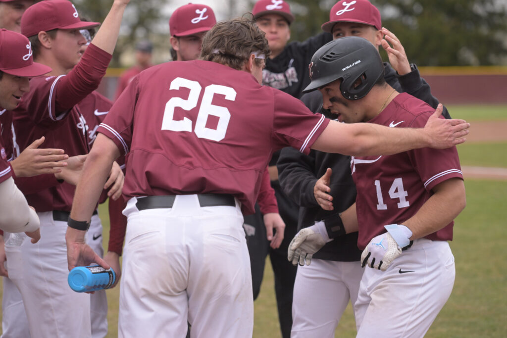 A baseball player is surrounded by his teammates in a celebration after a homerun hit. 